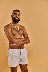 A shirtless man with a striking beard stands confidently, arms crossed, exuding strength and...