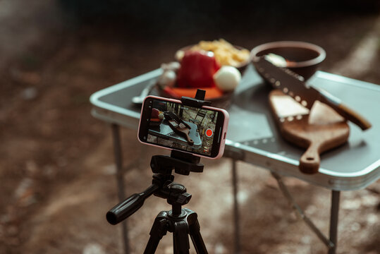 Sliced vegetables and a knife and cutting board are filmed with a phone camera outdoors in the woods