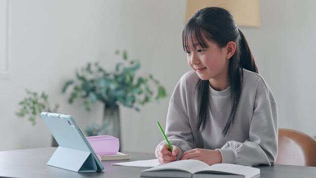 Elementary school girl studying at her desk at home while looking at a tablet PC.