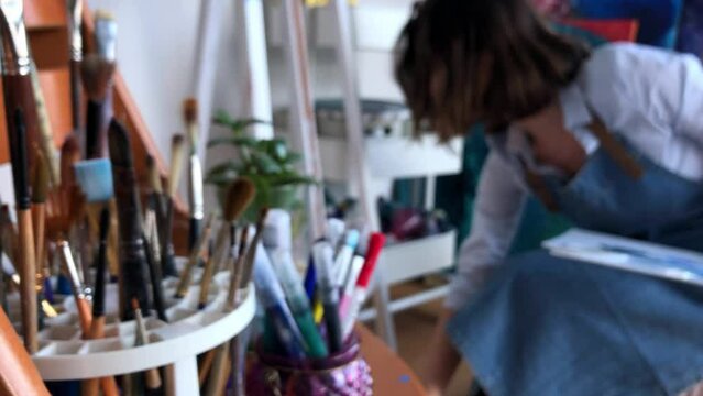 Female artist working in her studio. Getting ready to start painting. Cleaning up the mess, standing up. Blurred medium shot over instruments stand. High quality 2K footage.