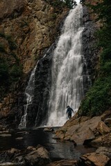 Vertical shot of a male tourist walking on rocky cliffs before a scenic waterfall