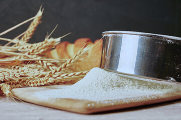 a loaf of bread,a sieve, coarse flour, grains and ears of wheat