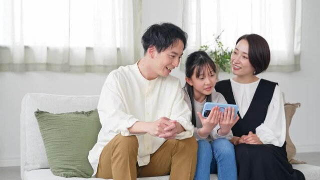 A family of an Asian girl and her parents looking at a smartphone screen.