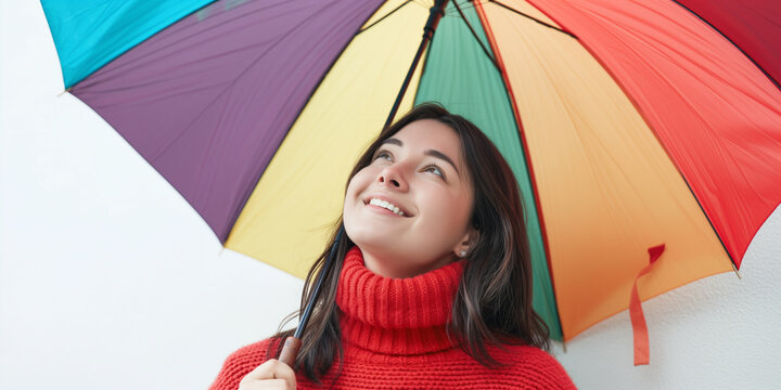 Happy smiling young woman with colorful umbrella in autumn day looking up over white background wearing a red knitted sweater professional photography.