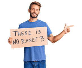 Handsome blond man with beard holding there is no planet b banner smiling happy pointing with hand and finger to the side
