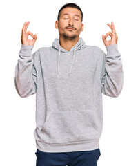 Handsome man with tattoos wearing casual sweatshirt relax and smiling with eyes closed doing meditation gesture with fingers. yoga concept.