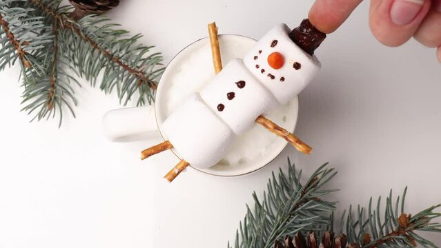 Christmas morning with a cup of hot chocolate (or cappuccino) featuring cheerful snowman marshmallows . the snowman is lying in a mug. spruce branches and wooden sleigh