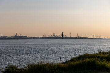 Beautiful windmills in the port of Rotterdam. Beautiful sunset on the sea coast. The Blue North Sea and Water surface. The lighthouse and shore are lit by the sunset sun. - obrazy, fototapety, plakaty