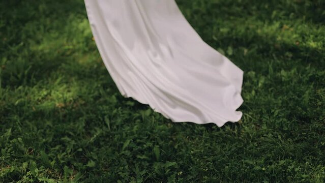 A girl in a long white dress runs through the grass. Shooting her legs in slow motion