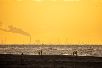 People walk on the shores of the North Sea. Beautiful orange, yellow sunset. The sea is in the background. Beautiful storm and waves. Yellow sand in the foreground.
