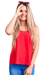 Young beautiful blonde woman wearing sleeveless t-shirt and sunglasses doing ok gesture with hand smiling, eye looking through fingers with happy face.