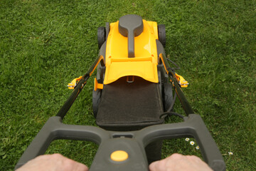 Yellow lawn mower on the spring green grass in the yard