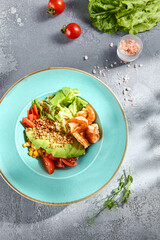 Top view of an avocado salad bowl with smoked salmon and mixed vegetables, on a textured table
