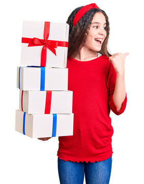Cute hispanic child girl holding gift pointing thumb up to the side smiling happy with open mouth
