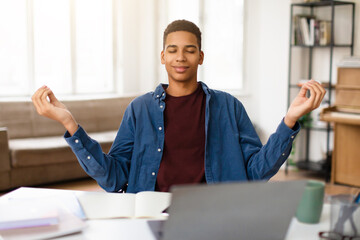 Relaxed black teen guy meditating at desk with laptop