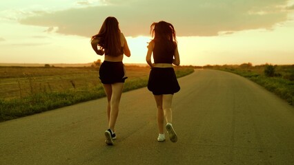 Athletic young women running along an asphalt road at sunset, healthy fitness lifestyle. Girls run...