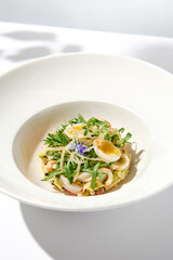 Healthy salad with squid and avocado on white plate with harsh shadows. Calamari salad with vegetables and eggs on white background with shadows of leaves. Summer food menu.