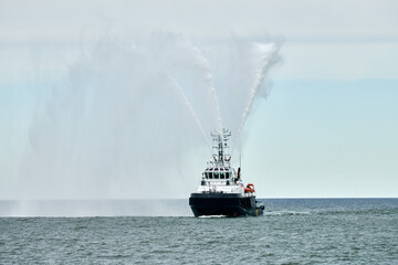 Fireboat ship sails on open sea directing jets of water to sides demonstrating bravery water salute, nautical spectacle of russian maritime strength at Russian naval forces parade