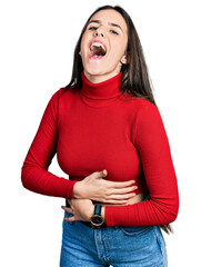 Young brunette teenager wearing red turtleneck sweater smiling and laughing hard out loud because...