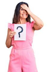 Young beautiful brunette woman holding question mark stressed and frustrated with hand on head, surprised and angry face