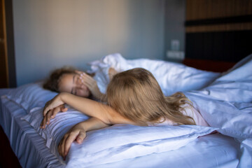 Side view of two little blonde sisters girls after a night's sleep on a large white bed in a...