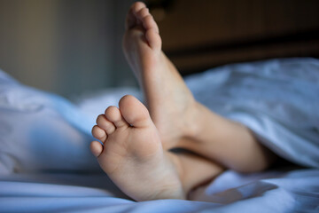 Close-up of the feet of a small child who fell asleep on a huge white bed, symbolizing the concept...