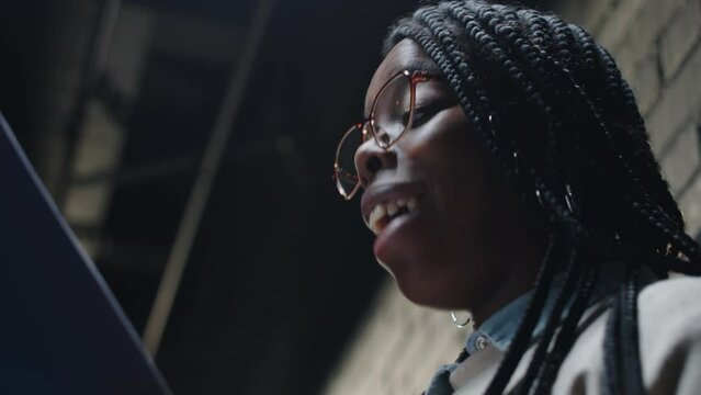 Low angle medium closeup of young African American female comedian performing standup monologue standing under projector light on dark stage