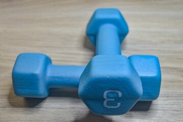 Closeup of a pair of blue 3 kilogram dumbbells on a wooden background