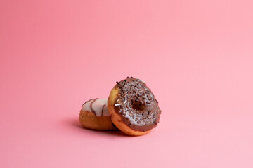 chocolate glazed donut supported on another one on pink background - obrazy, fototapety, plakaty