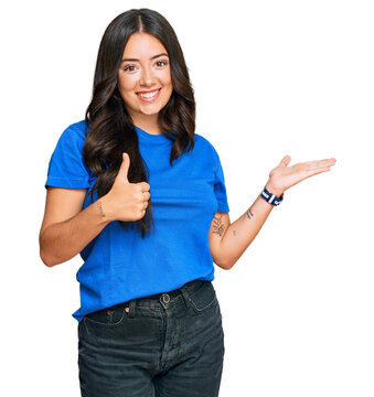 Beautiful brunette young woman wearing casual clothes showing palm hand and doing ok gesture with thumbs up, smiling happy and cheerful