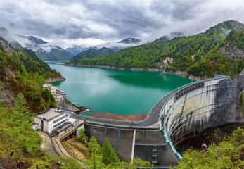 Stormy skies and snowcapped mountains next to a huge hydroelectric dam (Kurobe Dam, Japan)