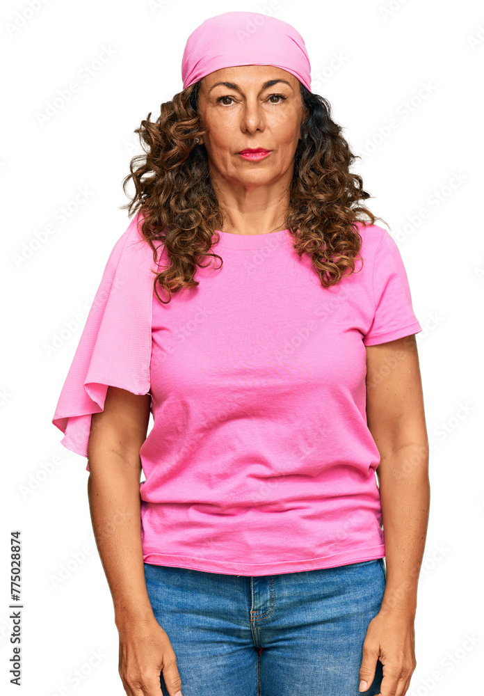 Poster middle age hispanic woman wearing breast cancer support pink scarf with serious expression on face. 