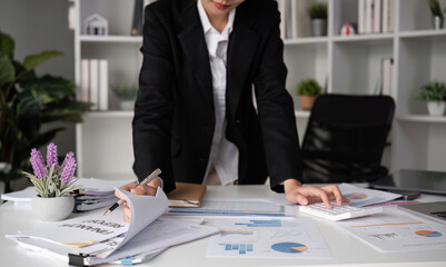 A young accountant calculates financial figures and company spending graphs using a calculator and...