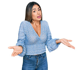 Young hispanic woman wearing casual clothes clueless and confused expression with arms and hands...
