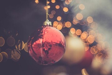 Closeup of a shiny red Christmas tree ornament with orange bokeh around it on a blurred background