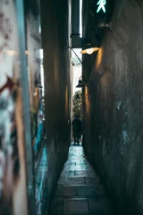 Cercles muraux Ruelle étroite Vertical shot of a person walking down the stairs of a very narrow alleyway between buildings