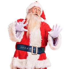 Old senior man with grey hair and long beard wearing traditional santa claus costume afraid and terrified with fear expression stop gesture with hands, shouting in shock. panic concept.