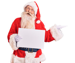 Naklejka premium Old senior man with grey hair and long beard wearing santa claus costume holding banner celebrating victory with happy smile and winner expression with raised hands