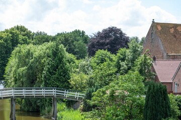 Fototapeta premium Scenic shot of green trees, bridge over a canal and rural houses under the clouds
