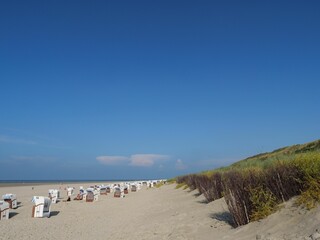 Fototapeta na wymiar Beach chairs on the sand under blue sky in Spiekeroog town, Germany