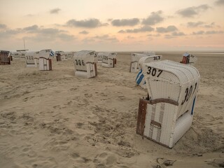 Numbered beach chairs on the sand of an island under cloudy sky at sunset in Spiekeroog town