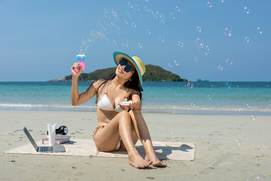 Beautiful Asian woman in bikini enjoy playing with a soap bubbles on the beach on vacation.