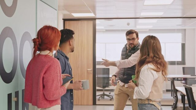 An authoritative figure reprimands three casually conversing employees, pointing them towards their work areas in a modern office environment. 