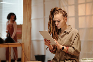 Young serious woman with dreadlocks using tablet while gathering online information about renovation of location in front of camera - 775038074