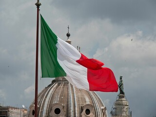 Italian flag waving, with Trajan Column and church dome of Santa Maria di Loreto in the background