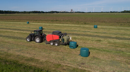 Schwarzer Treker oder Traktor mit einer roten Stroh Festkammerpresse bei der Strohernte auf einem gemähten Feld - 775039237
