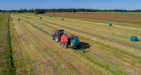 Schwarzer Treker oder Traktor mit einer roten Stroh Festkammerpresse bei der Strohernte auf einem gemähten Feld