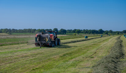 Schwarzer Treker oder Traktor mit einer roten Stroh Festkammerpresse bei der Strohernte auf einem gemähten Feld - 775039412