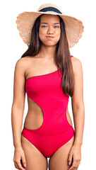 Young beautiful latin girl wearing swimwear and summer hat puffing cheeks with funny face. mouth inflated with air, crazy expression.