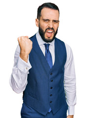 Young man with beard wearing business vest angry and mad raising fist frustrated and furious while shouting with anger. rage and aggressive concept.